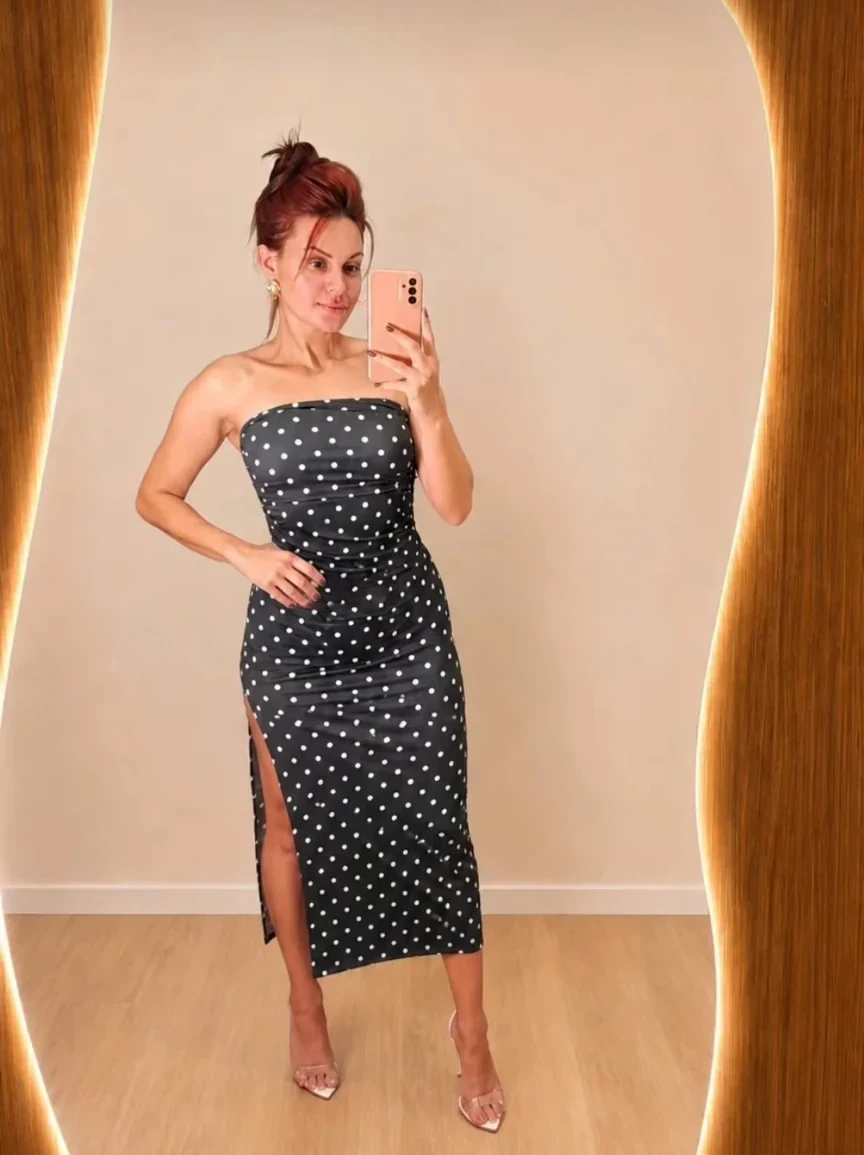 Modelo veste vestido preto de poás diante do espelho iluminado da Linda Moda Feminina